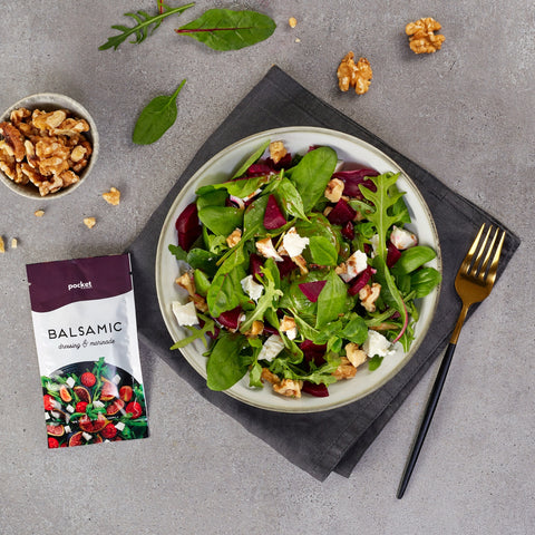 Single serve balsamic salad dressing packet next to bowl of salad and a small bowl of walnuts.